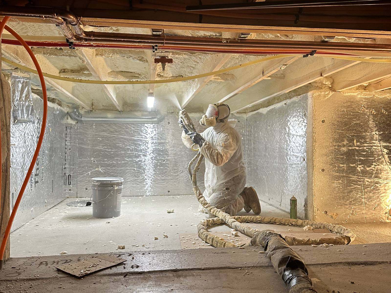 Installer in protective suit spraying foam insulation in a crawl space